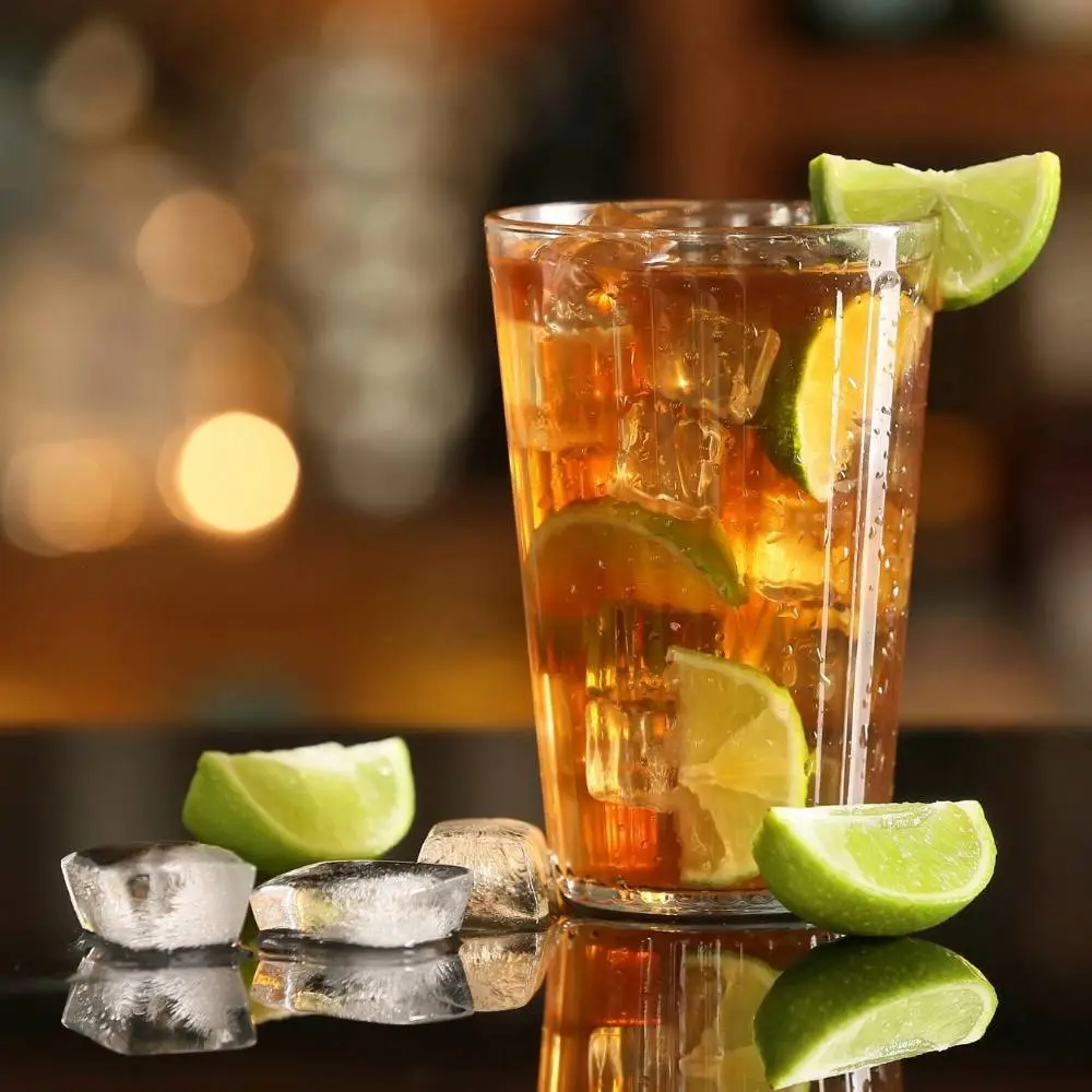 A Long Island ice tea cocktail on a black bar with lime wedges around it.